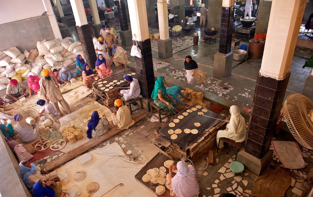 Overview of volunteers cooking and rolling rotis in large kitchen space