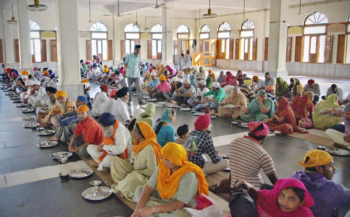 Rows of diverse people dining together in Langar hall